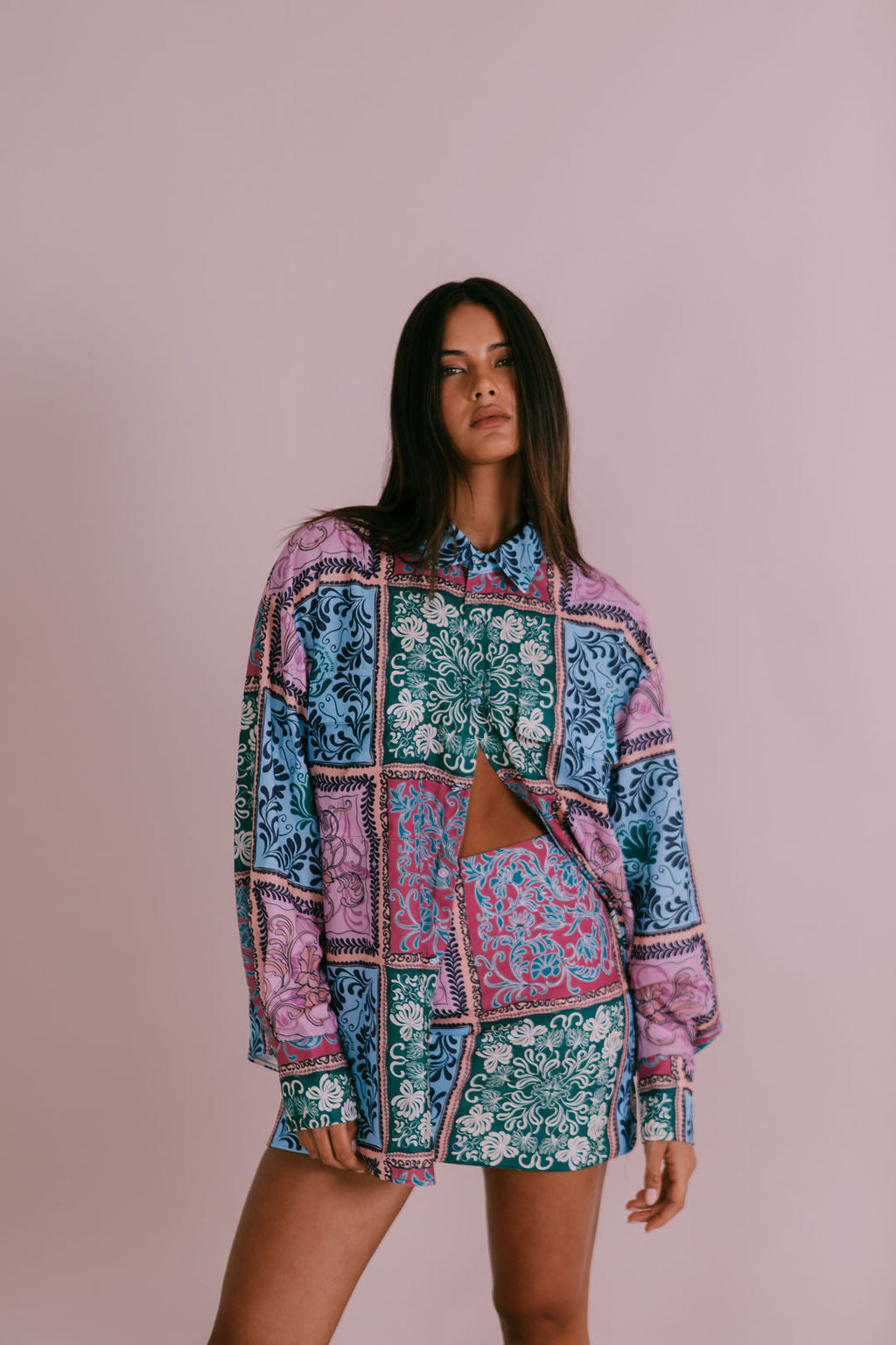 A female model wearing an oversized, multicolored paisley tile print shirt with two pockets and a classic collar.